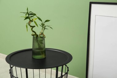 Yeşil duvarın yanındaki sehpanın üzerinde bambu saplı vazo, yakın plan.