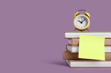 Leylak arkaplan üzerinde boş yapışkan not olan farklı kitapların üzerindeki alarm saati