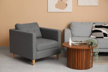 Masası, gri koltuğu ve bej duvarın yanındaki koltuğu olan bir oda.