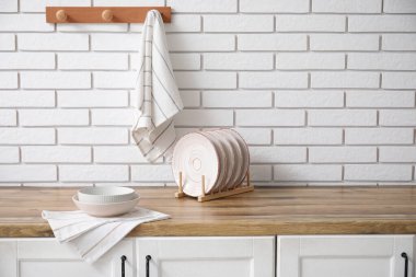 Temiz tabaklar, tabaklar ve peçeteler mutfaktaki beyaz tuğla duvarın yanında.