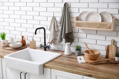 Mutfaktaki beyaz tuğla duvarın yanında lavabo ve temiz peçetelerle tezgahlar.