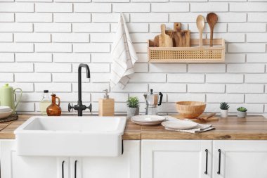 Temiz peçeteler ve farklı bulaşık takımları mutfaktaki beyaz tuğla duvarın yanındaki tezgahlarda.