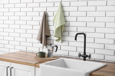 Tezgahta fincanı olan gayzer kahve makinesi ve mutfakta beyaz tuğla duvara asılı temiz peçeteler.