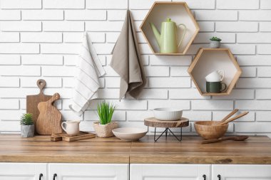 Tezgahlarda farklı bulaşık takımları ve mutfaktaki beyaz tuğla duvara asılı temiz peçeteler.