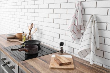 Tezgahlardaki aletler ve elektrikli soba ve mutfaktaki beyaz tuğladan duvara asılı temiz peçeteler.