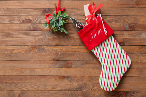 Рождественский носок с подарком, елка, леденцы и веточка омелы на деревянном фоне