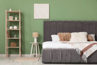 Yatak odasındaki yeşil duvarın yanında büyük, rahat bir yatak ve raf var.