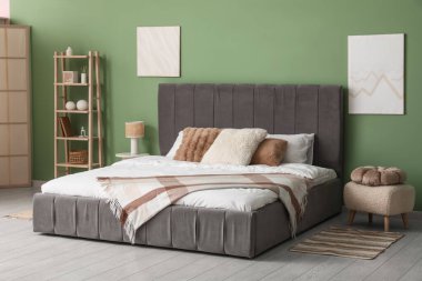 Yatak odasındaki yeşil duvarın yanında büyük, rahat bir yatak ve raf var.