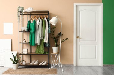 Koridorun iç tarafındaki bej duvarın yanında giysi olan zemin lambası ve askısı.