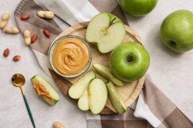 Wooden plate with fresh apples and bowl of sweet peanut butter on white background