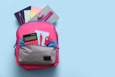 Mavi arka planda farklı kırtasiye malzemeleriyle süslü okul çantası.