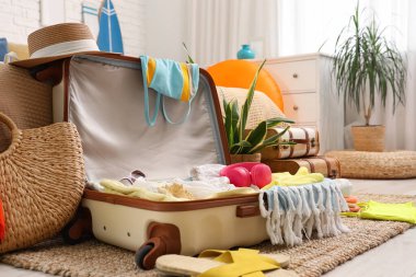 Yatak odasının yanında üzerinde giysiler, plaj aksesuarları ve kulaklıklar olan bavulu aç.