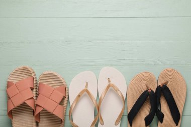 Yeşil ahşap arka planda farklı tarz parmak arası terlikleri olan kompozisyon, yakın plan.