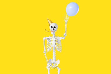 Parti şapkalı insan iskeleti sarı arka planda balon tutuyor, yakın plan.