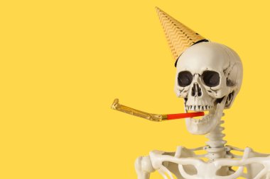 Parti şapkalı insan iskeleti, sarı arka planda parti düdüğü, yakın plan.