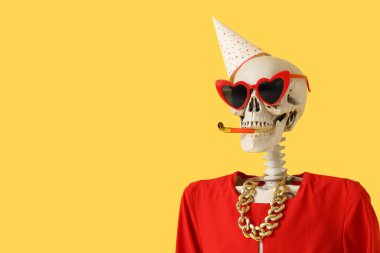 Parti şapkalı insan iskeleti, güneş gözlüğü ve sarı arka planda parti düdüğü çalan elbise, yakın plan.