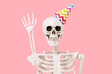 Parti şapkalı insan iskeleti pembe arka planda el kaldırıyor, yakın plan.