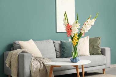 Rahat bir kanepe, masa ve vazo, oturma odasının içinde gladyatör çiçekleri, yakın plan.