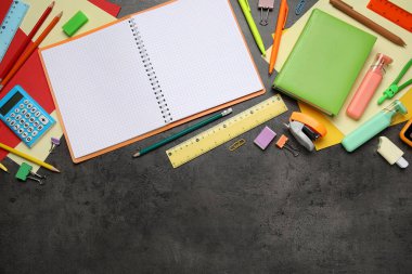 Boş bir defter ve siyah grunge arka planında farklı okul malzemeleri.