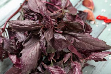 Sarımsaklı taze mor fesleğen yaprakları ve mavi ahşap arka planda kırmızı biber, yakın plan.