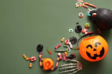 Balkabağı şeklinde kazanlar Cadılar Bayramı için şekerler, yeşil arka planda iskelet ve kafatası.