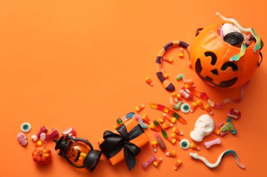 Cadılar Bayramı için şekerli balkabağı şeklinde kazan, turuncu arka planda fener ve hediye kutusu