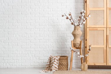 Ahşap dolap, hasır sepet ve oturma odasının içinde pamuk çiçekli vazolar.