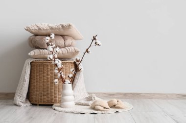 Oturma odasının iç tarafındaki beyaz duvarın yanında pamuk çiçekli sepet, yastıklar ve vazolar.