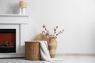 Şömine, hasır sepet ve vazo. Oturma odasının iç tarafındaki beyaz duvarın yanında pamuk çiçekler var.
