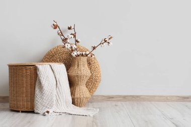 Hasır sepet, puf ve vazo, oturma odasının iç tarafındaki beyaz duvarın yanında pamuk çiçekler.