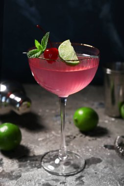 Bir bardak lezzetli Cosmopolitan kokteyli. Üzerinde kiraz ve limon var. Mavi arka planda.