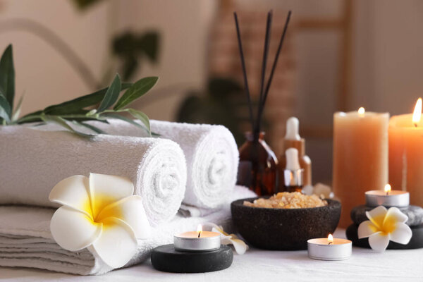 Plumeria цветы, чистые полотенца и горящие свечи на диване в ванной комнате, крупным планом