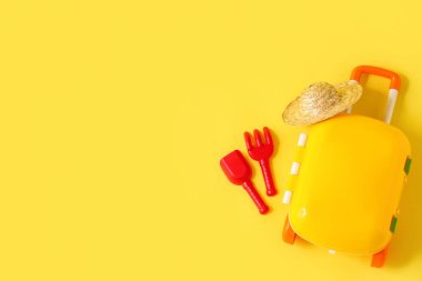 Çocuk bavulu, şapka, oyuncak tırmık ve sarı arka planda kürekle kompozisyon