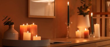 Karanlık odadaki çekmecelerin üzerinde okaliptüslü mumlar ve vazolar yakıyor.