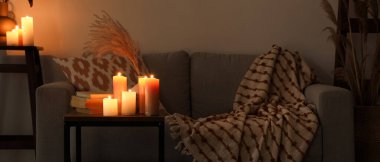 Mumlar, vazolar, otlar ve karanlık oturma odasının iç tarafındaki masada kitaplar.