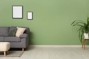 Yeşil duvarın yanında rahat kanepe, puf ve çiçekli şık bir oturma odası.