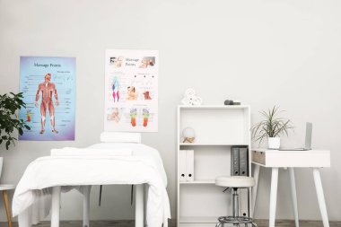 Çalışma yeri, kanepe, raf ünitesi ve modern tıp merkezinin duvarlarında posterleri olan masaj terapistinin bürosu.