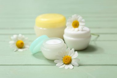 Kavanozlar dolusu papatya çayı ve yeşil ahşap arka planda çiçekler.