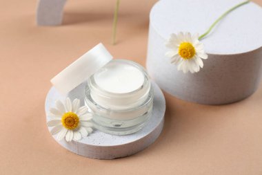 Dekoratif podyumlar bir kavanoz papatya kozmetik kremi ve kahverengi arka planda çiçekler, yakın plan