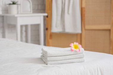 Otel odasındaki yatağın üzerinde pembe Plumeria çiçeği olan bir yığın temiz havlu.