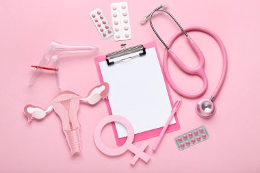 Kağıt uterusu olan pano, kadın sembolü, steteskop, jinekolojik spekulum ve pembe arka planda haplar.