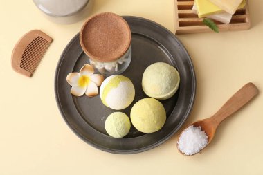 Tepsi, banyo bombaları ve sarı arka planda bir çiçek kompozisyonu.