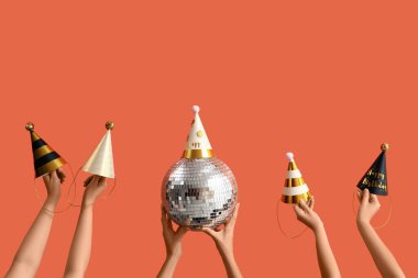 Turuncu arka planda disko topu ve parti şapkası olan kadın elleri.