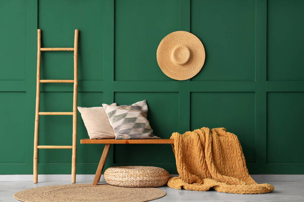 Wooden bench with pillows, plaid and ladder near green wall in room