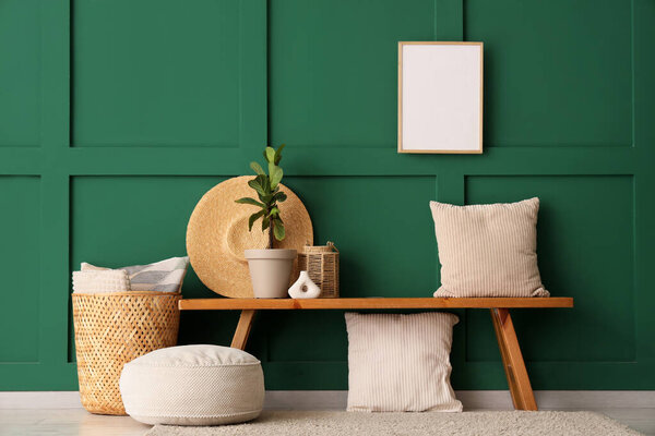 Wooden bench with pillows, wicker basket and houseplant near green wall in room