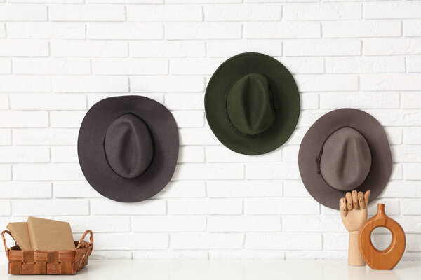 Стильные шляпы на стене из белого кирпича над полкой в комнате
