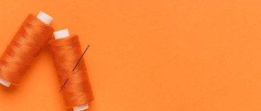 Turuncu arkaplan üzerinde iplik ve iğne makaraları metin için boşluk, üst görünüm