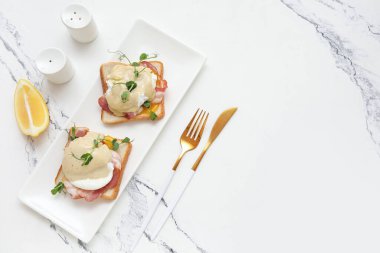 Lezzetli yumurta Benedict, limon dilimi ve mermer arka planda çatal bıçak.