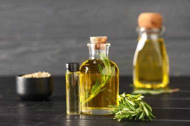 Siyah ahşap arka planda taze biberiye ile gerekli yağ şişeleri