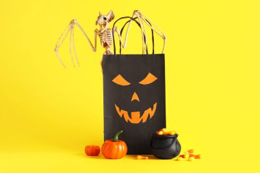 Lezzetli Cadılar Bayramı şekerli kazan mısır, balkabağı, yarasa iskeleti ve sarı arka planda kağıt torba
